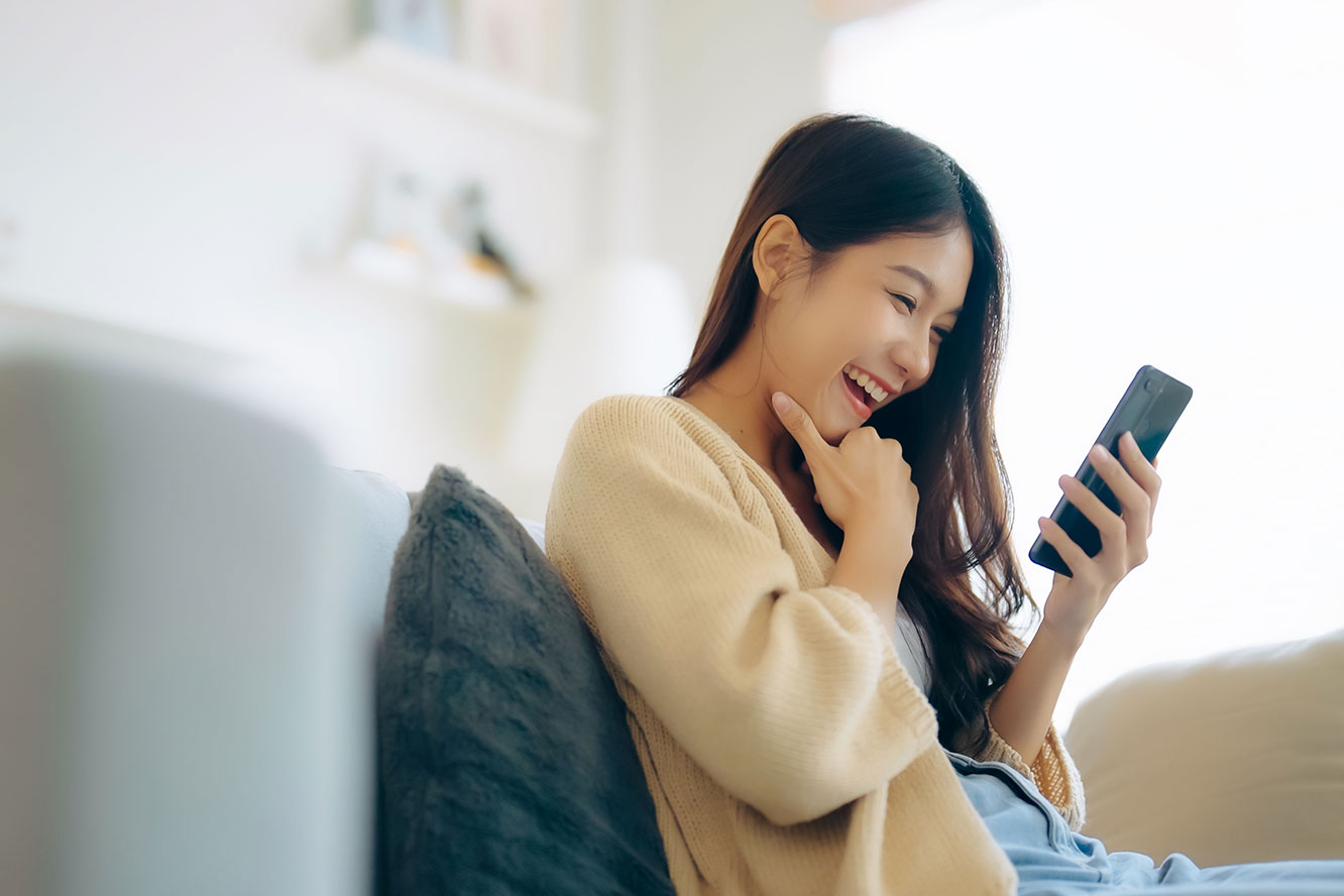 Perempuan tersenyum melihat ponsel